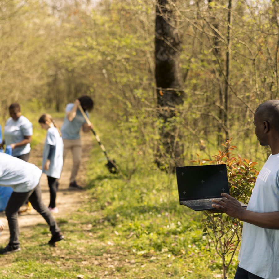 African american activist checks isolated mockup on laptop, participates in collecting rubbish from the forest area. Environmental volunteer works to protect the ecosystem, community outreach.